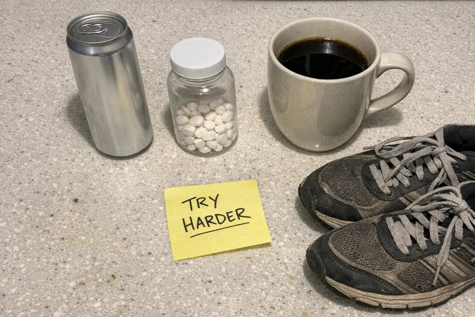Overhead phone photo of an energy drink can, B12 tablets, a large coffee mug, walking shoes and a sticky note