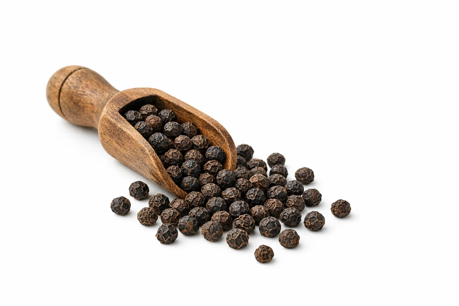 Whole black peppercorns spilling from a wooden scoop